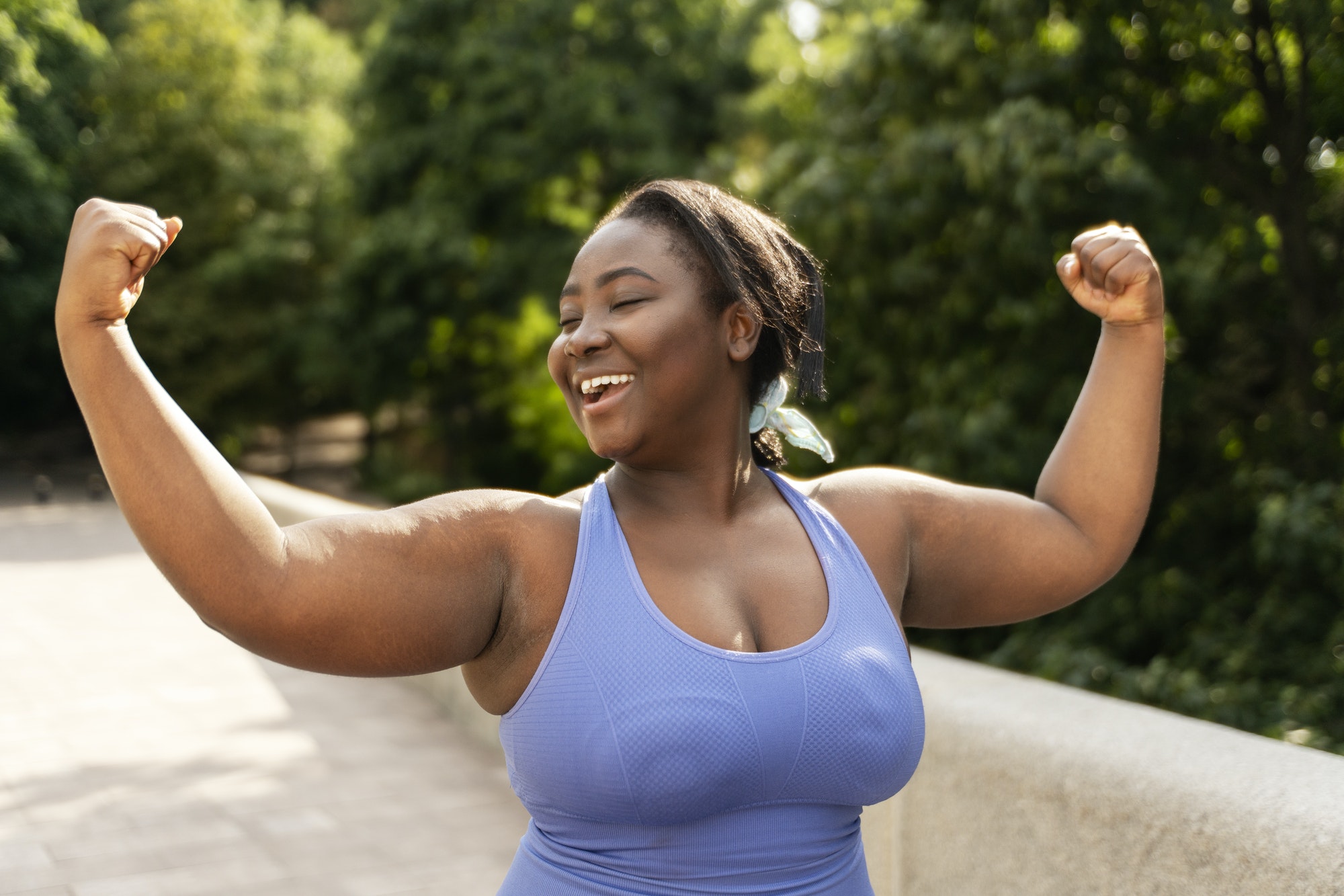 Beautiful smiling African American woman in sportswear showing biceps exercising on the street