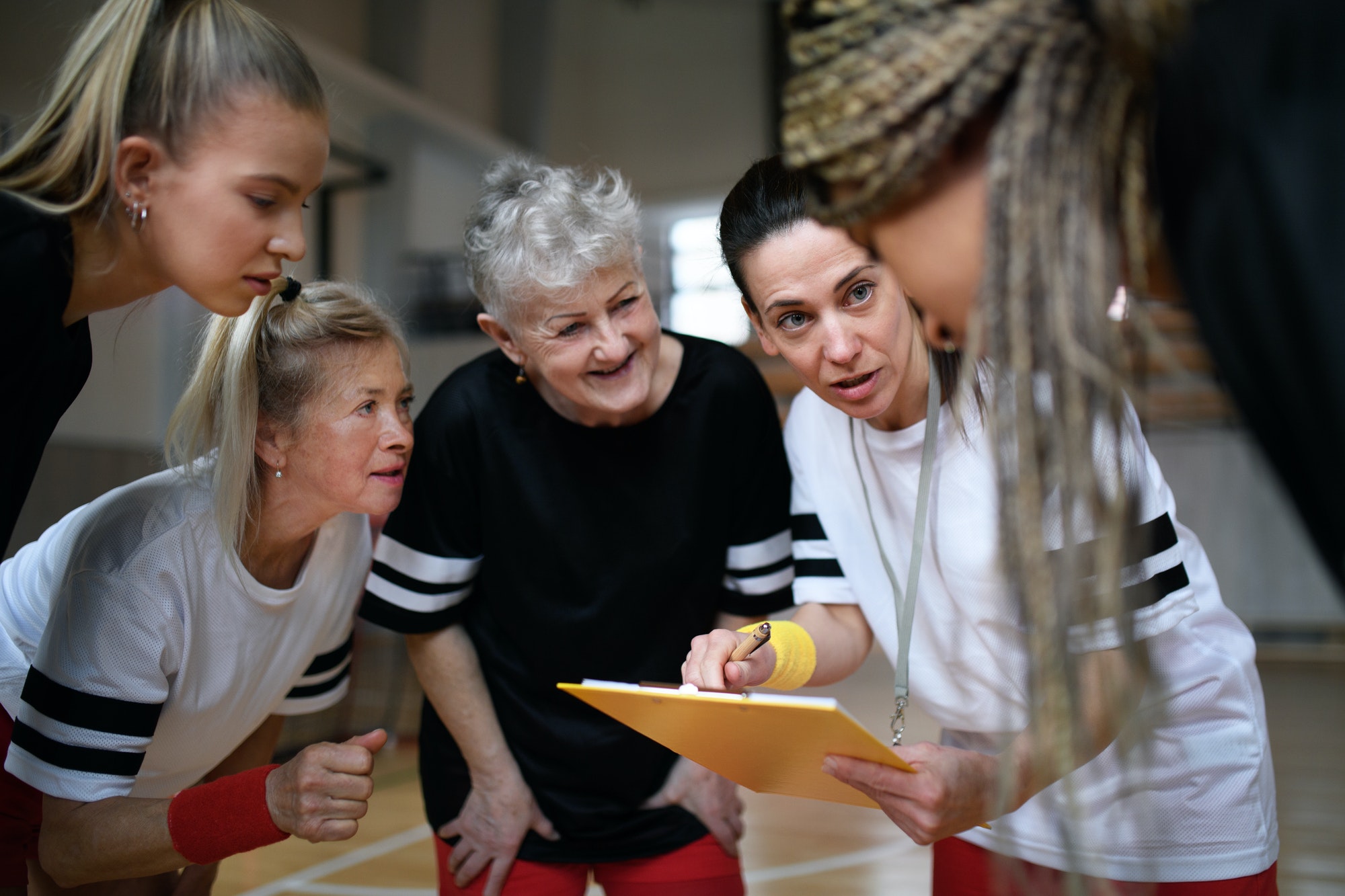 Female sport coach with clipboard discussing tactics with young and old women team training for