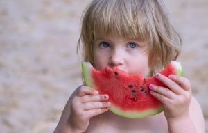 a cute little girl eats watermelon with an appetite and enjoys life in the summer.